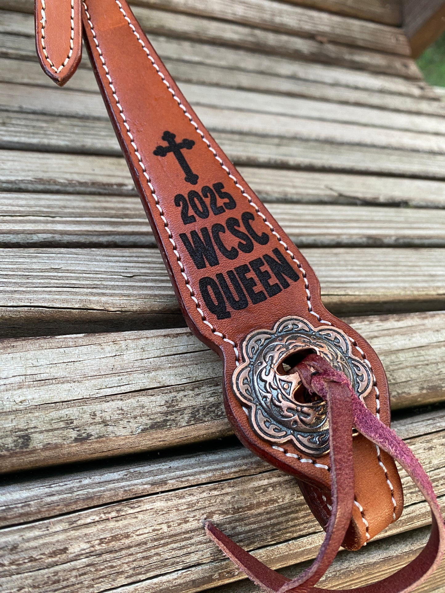 Closeup detail of brown leather equestrian headstall laser engraved cheek pieces for a rodeo queen with the year and a cross detail