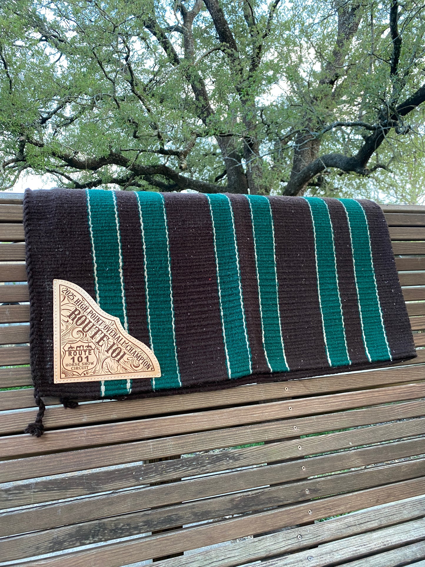 Striped blanket with a brand logo laser engraved on leather corners displayed on a wooden surface outdoors