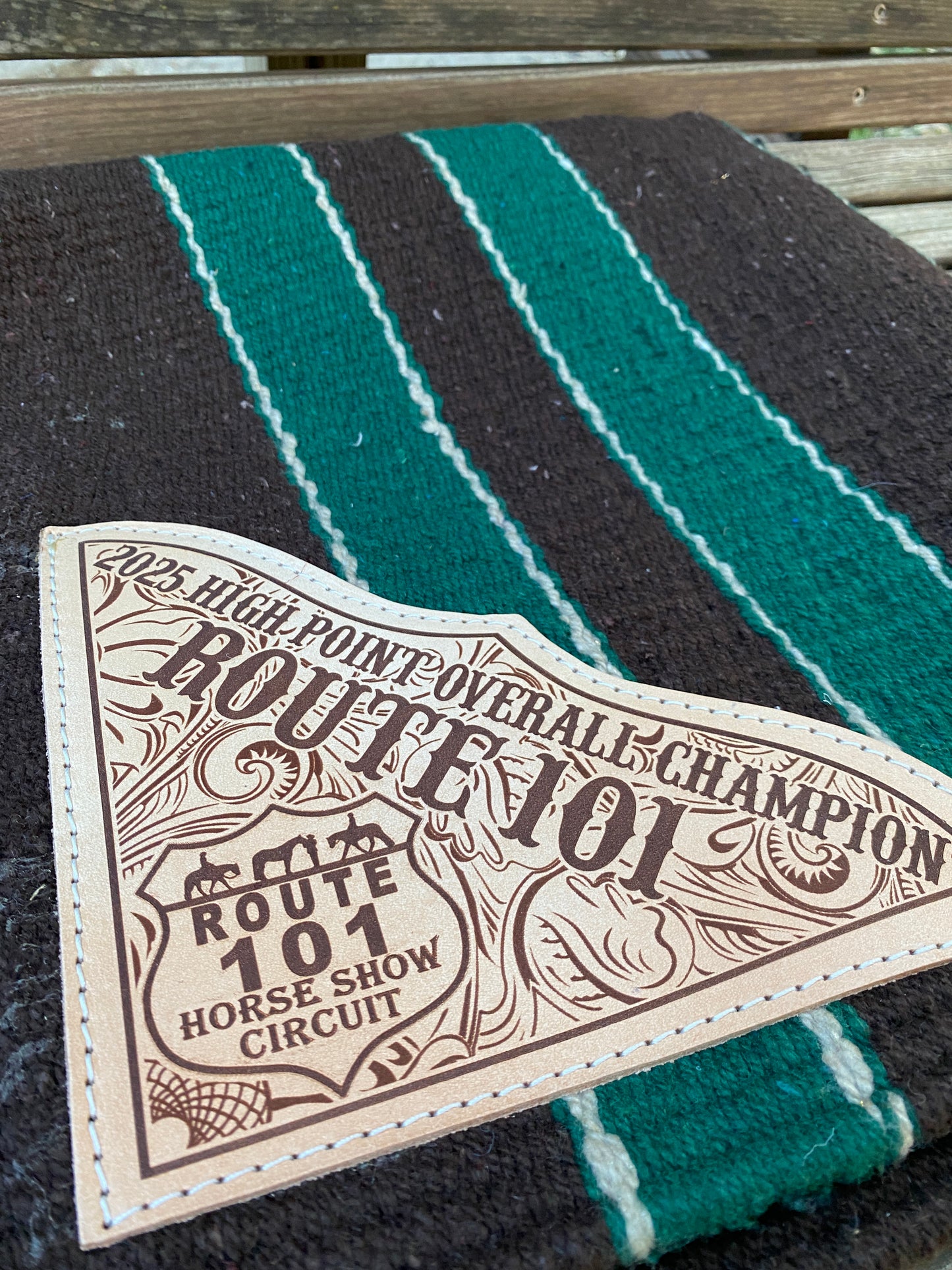 Close-up of a custom leather patch for a horse riding club with champion text on a green and brown striped saddle blanket