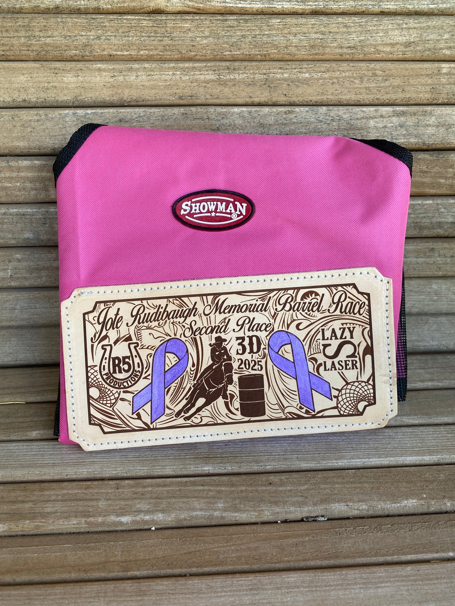 Pink award hay bag for horses with a branded leather patch showing western art and sponsorship logos for a barrel race