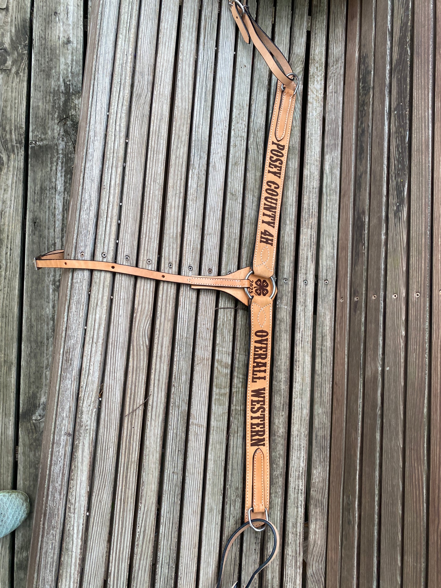 Leather custom tack breast collar with 'Posey County 4H' and 'Overall Western' branding on a rustic wooden surface
