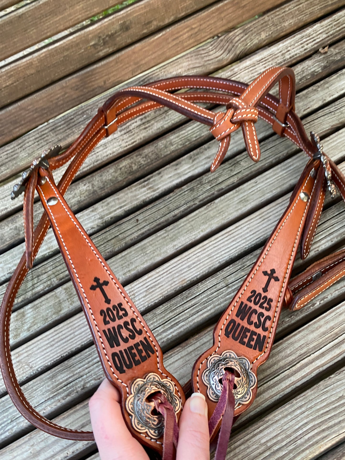 Brown leather browband headstall with engraved trophy cheek pieces and slotted conchos displayed on a wooden surface