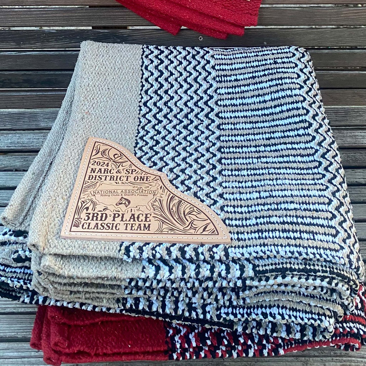 Folded custom saddle pads showing woven texture and custom engraved leather corner detail.