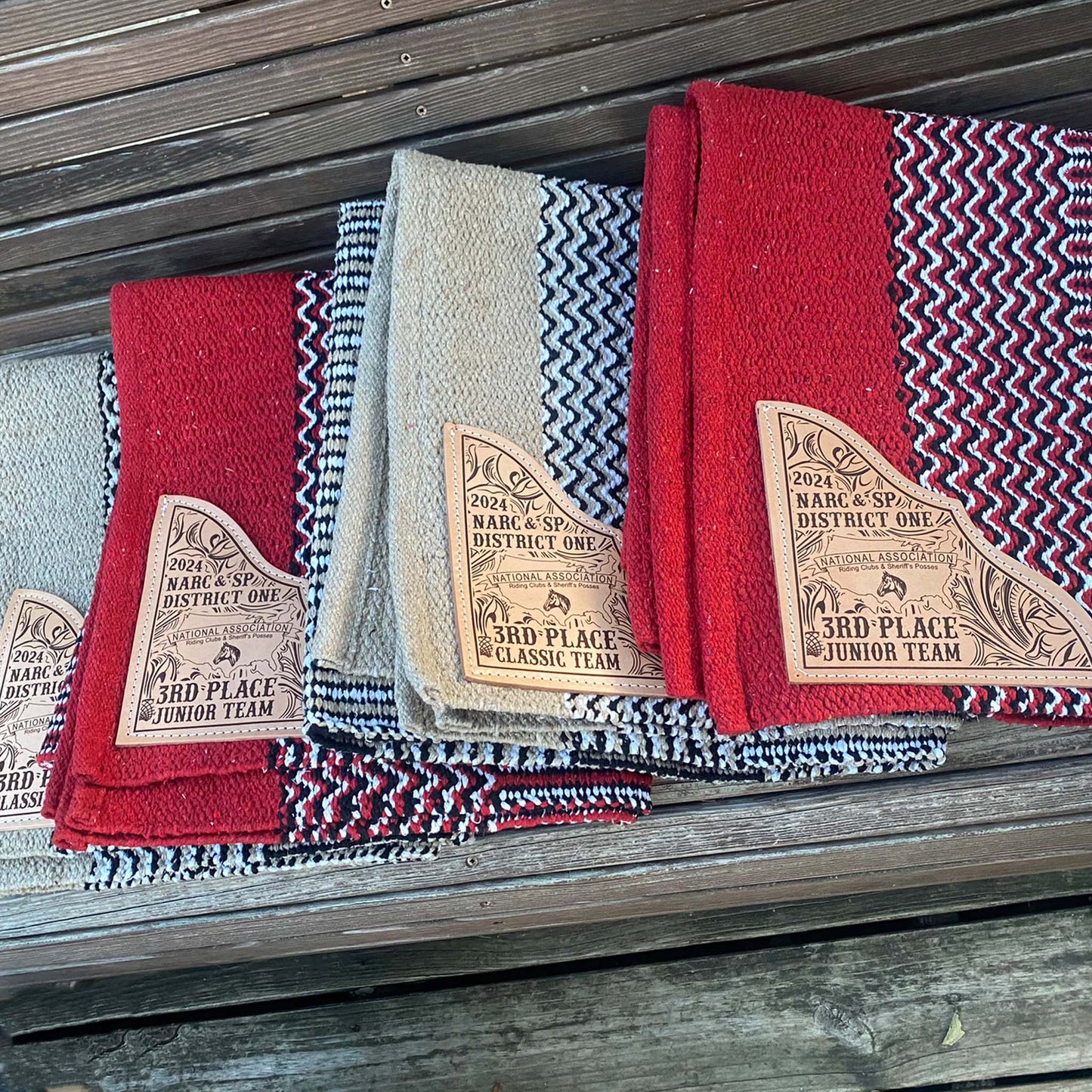 Stack of navajo pattern saddle blankets on shelf showing engraved leather corners and vibrant edge colors.