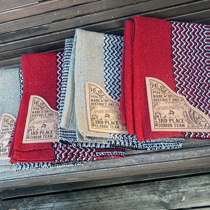 Stack of navajo pattern saddle blankets on shelf showing engraved leather corners and vibrant edge colors.