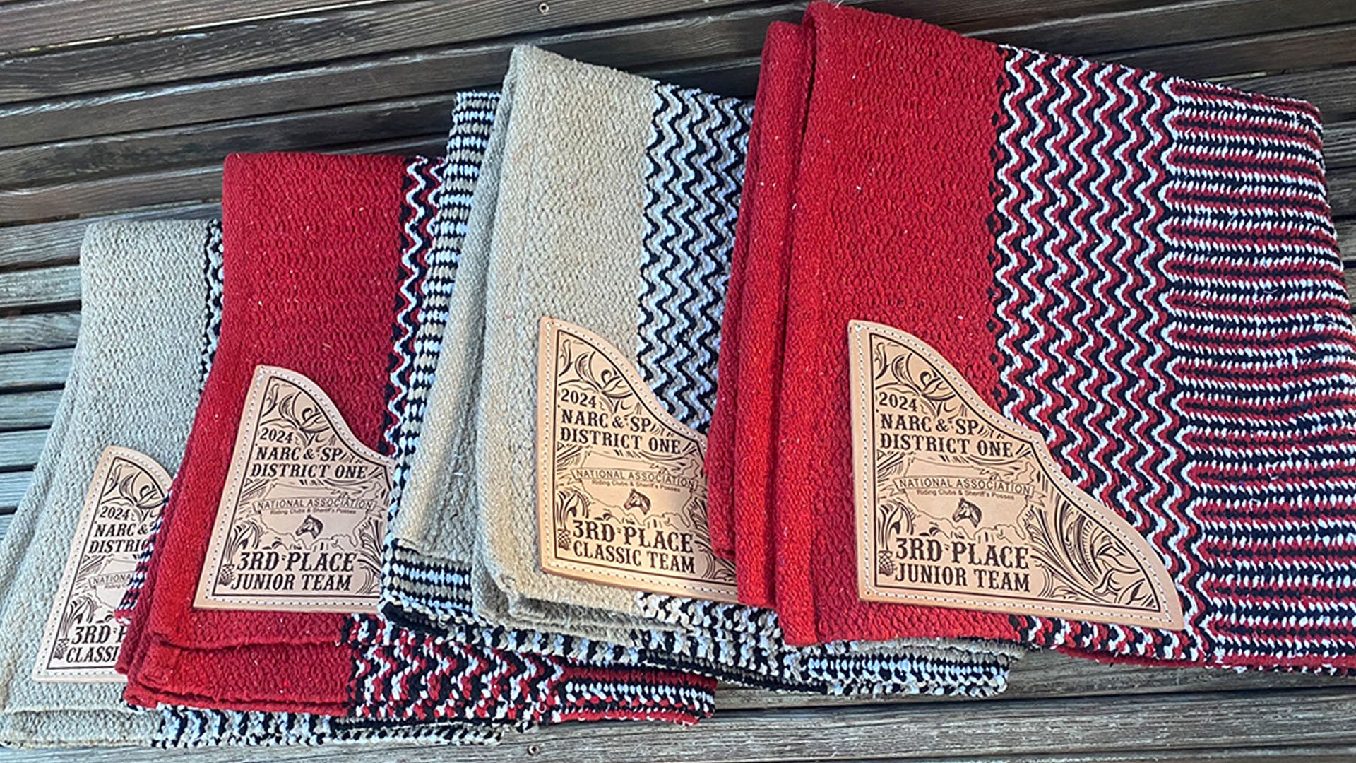 Display of several navajo pattern saddle blankets with riding club Team award text laser engraved on leather corners.