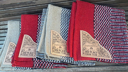 Display of several navajo pattern saddle blankets with riding club Team award text laser engraved on leather corners.