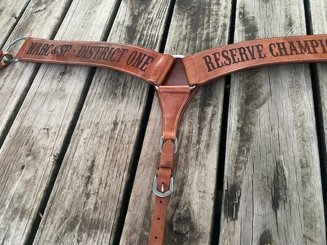 Custom trophy breast collar with laser etched text on a wooden surface