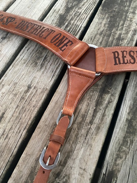Closeup of a custom breast collar center ring with engraved text on a wooden surface