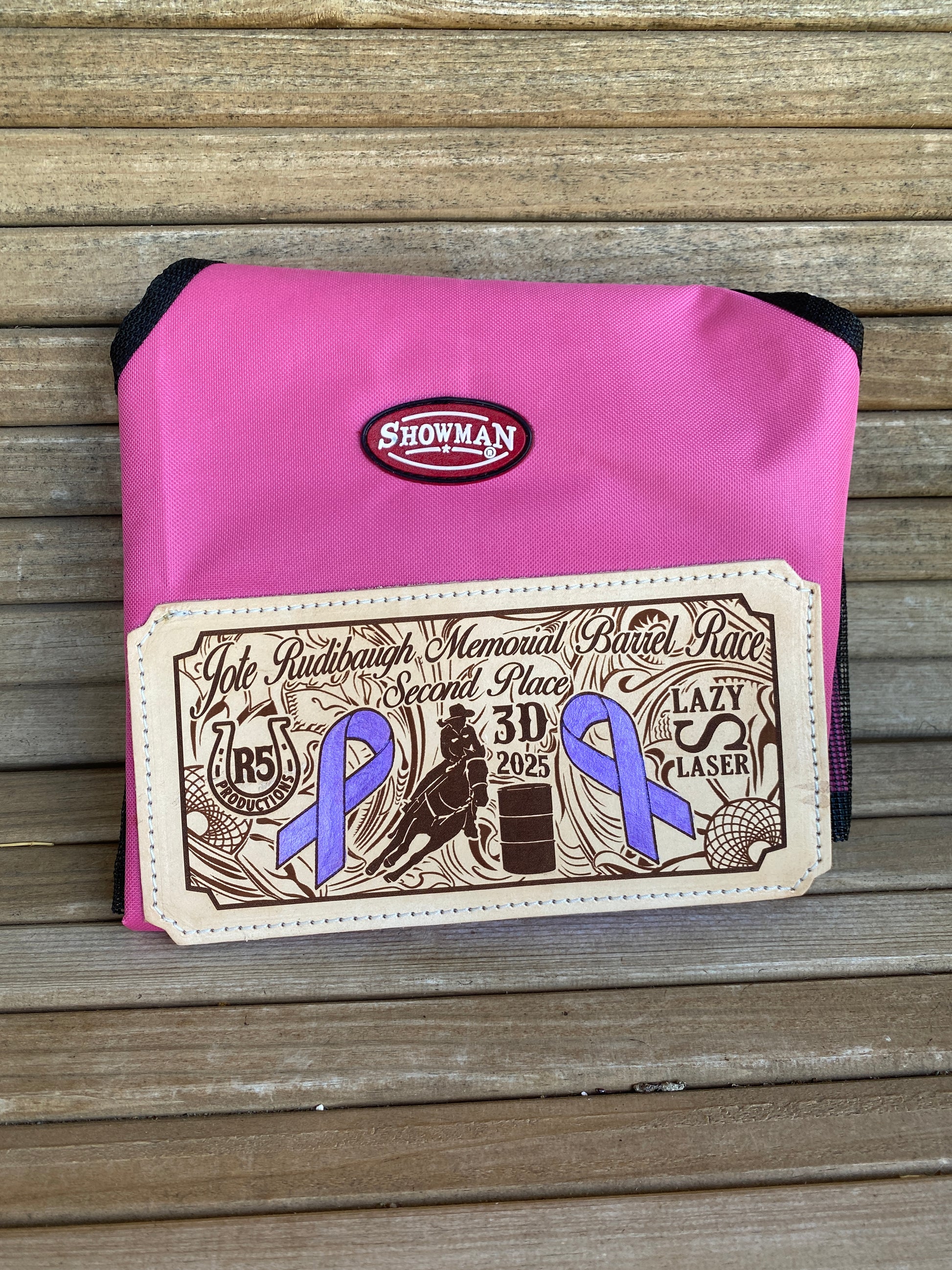 Pink award hay bag for horses with a branded leather patch showing western art and sponsorship logos for a barrel race