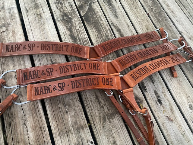 Set of 3 Western leather custom breast collars with dark lasered text on a rustic wooden surface