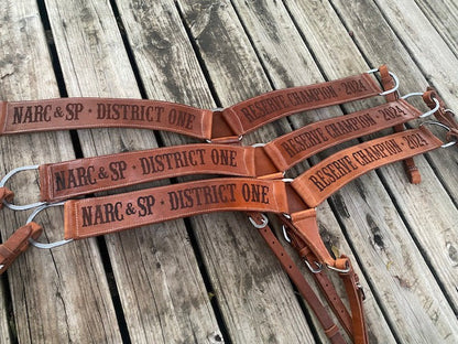 Set of 3 Western leather custom breast collars with dark lasered text on a rustic wooden surface
