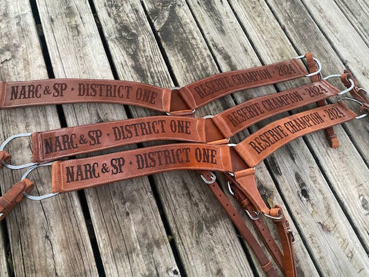 Set of 3 Western leather custom breast collars with dark lasered text on a rustic wooden surface