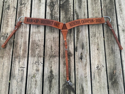 Brown leather breast collar with custom laser engraved award text on a wooden background