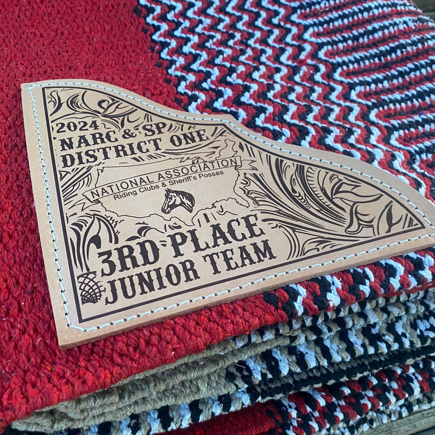 A custom laser engraved leather trophy patch sewn onto a woven saddle blanket.