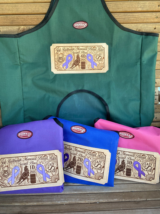 Group of trophy hay bags in different colors displayed on a wooden bench, highlighting the custom leather patches and painted purple cancer awareness ribbons on the designs