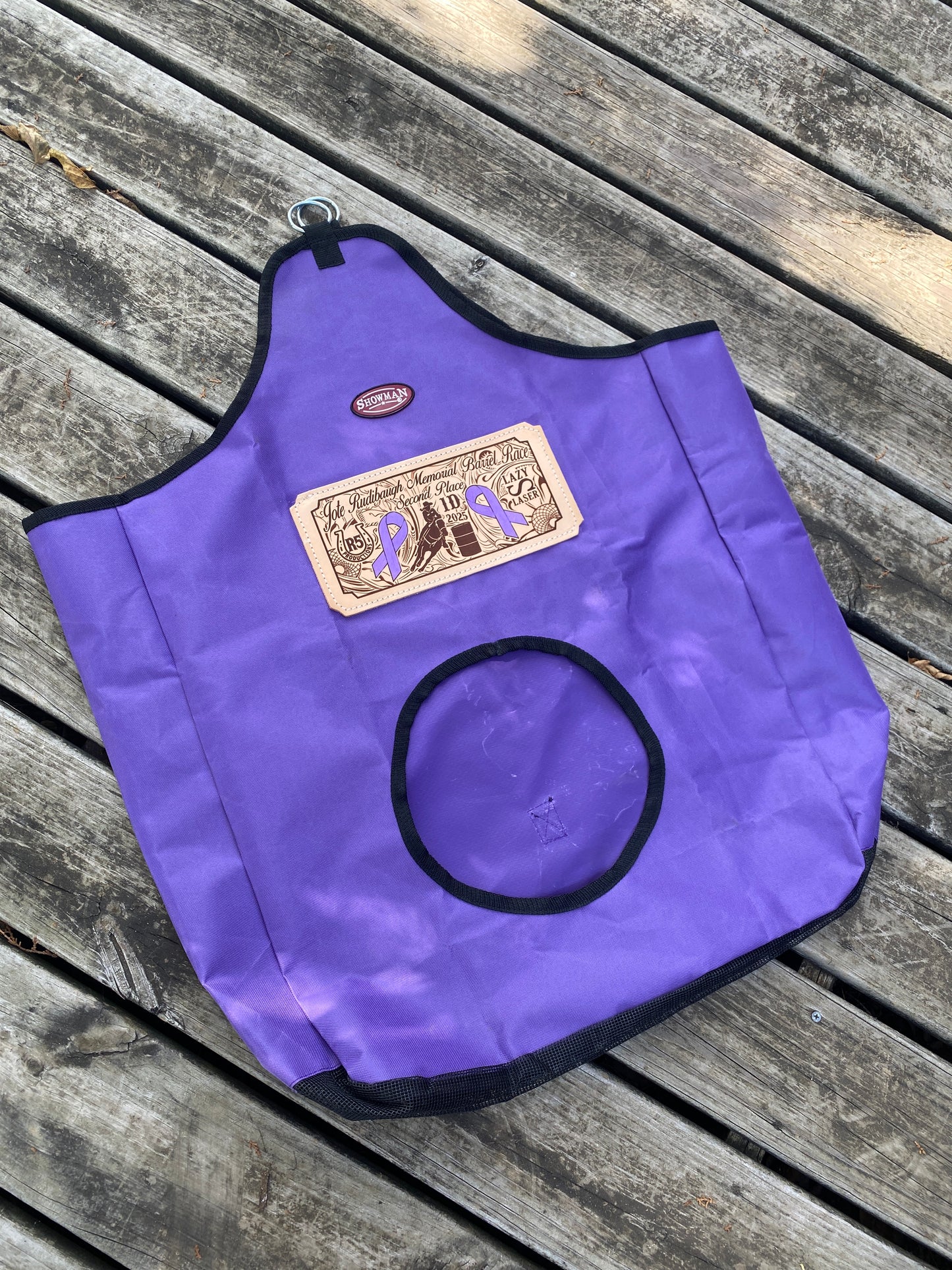 Custom purple nylon trophy hay bag with engraved leather patch on a rustic wooden surface